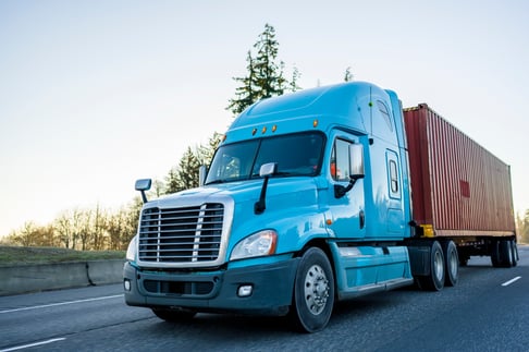 close up of blue big rig long haul semi truck transporting a shipping container down a highway