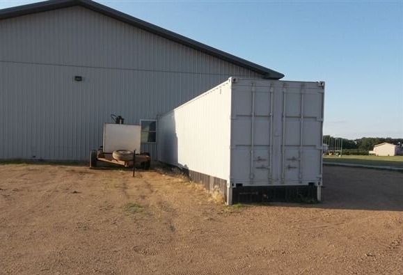 shipping container on foundation outside of large pole barn style shed