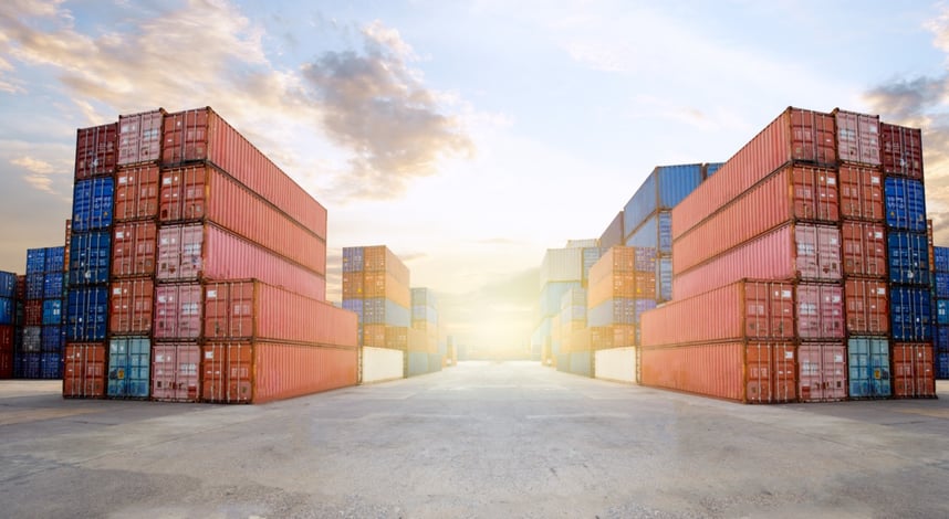 stacks of durable shipping containers in a shipping yard with the sun setting in the background