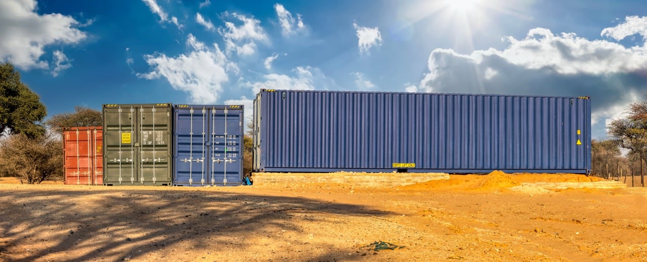 multiple shipping containers parked on a construction site with several containers sitting on the gravel and one on a foundation