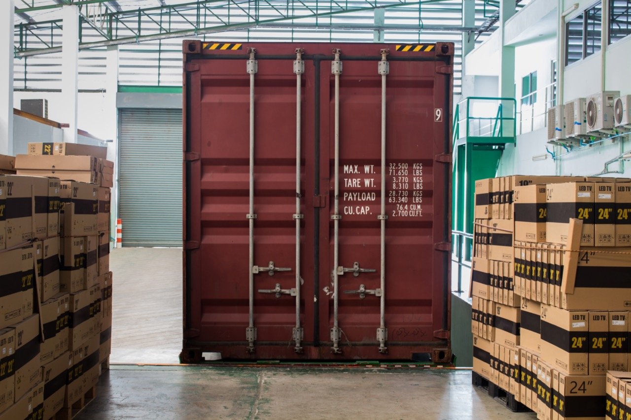 a red shipping container used for storage sitting on a warehouse floor near stacks of boxes